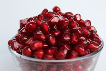 Fresh red seeds of pomegranate fruit, in transparent glass bowl, isolated on white background