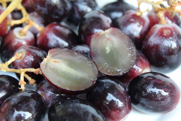 Halved dark purple or black grape with stem, seedless grape fruit, on white background