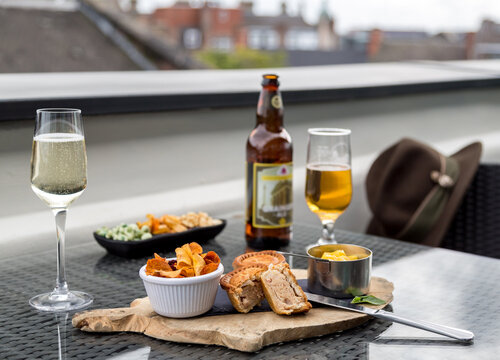 Some bar snacks consisting of mini pork pies, vegetable crisps or chips served with a cold beer and a glass of sparkling wine. Hotel guest. Room service.