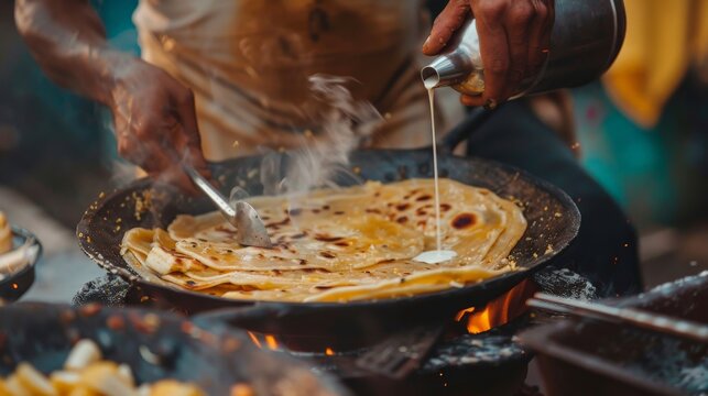 Indian street food. A man is cooking a paratha on a large skillet.