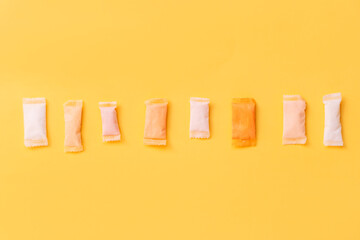 Multi-colored and different-flavored snus bags are laid out in a row on a yellow background.