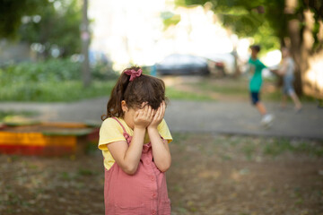 Upset lonely bullied little kid girl cries covering his eyes with his hands feels abandoned abused,...