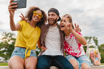 happy young company of smiling friends sitting in park