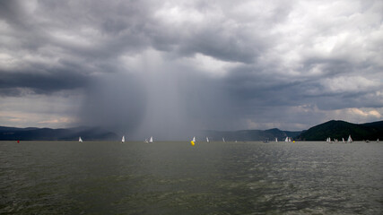 A sailing regatta unfolds on the Danube with a looming tempest in the backdrop