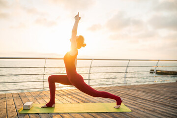 young slim beautiful attractive woman doing yoga in the morning on sunrise by sea