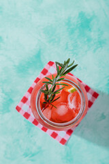 top view of refreshing summer drink cocktail with rosemary stick over red and white checkered paper