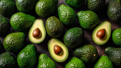 One sliced and many whole Avocados, a lot of green vegetables and lettuce leaves on the big table
