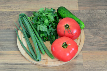 a wooden tray with a bunch of vegetables including tomato, parsley and cucumber