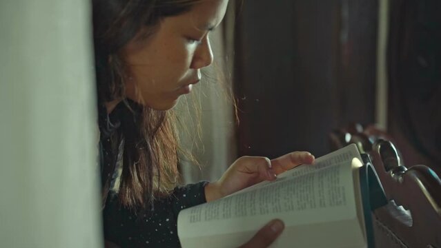 asian woman reading the Christian bible book on wooden table vintage room