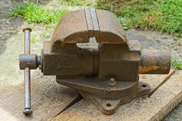 some heavy iron old ones for clamping, dirty manual mechanical industrial large vices stand on wooden boards during the day on the street