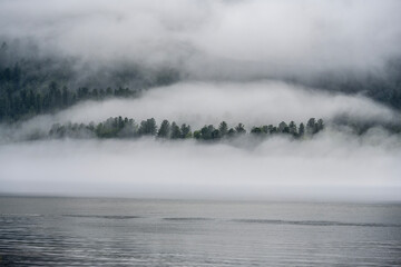thick morning fog on the lake against the backdrop of mountains landscape on Lake Teletskoye