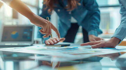 A close-up shot of hands pointing at documents on a table with team members engage in a collaborative business meeting, highlighting teamwork and strategic planning in an office setting.