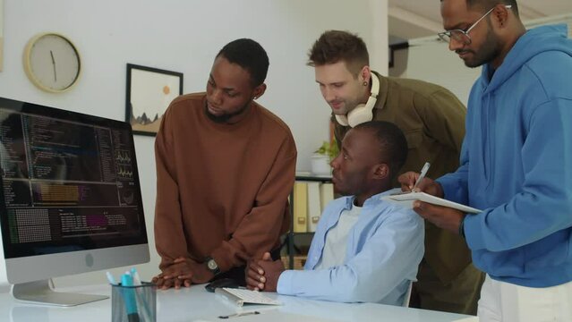 Medium shot of team of diverse programmers trying to fix bags in application code when looking at computer screen at office of startup company