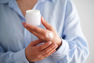 Hands in a blue shirt hold a jar of cream.