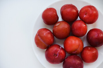 Red plums on a white background.  Plums on a plate. Washed fruits.
