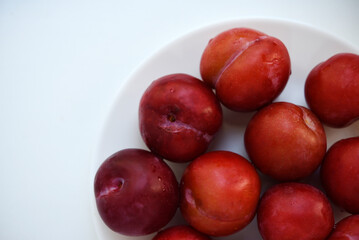 Red plums on a white background.  Plums on a plate. Washed fruits.