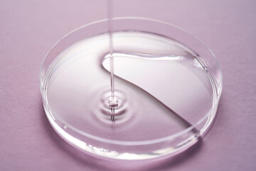 Serum or cosmetic oil flows into a transparent bowl on a purple background.