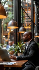 Obraz premium A focused entrepreneur in a suit works diligently on his laptop in a modern, stylish café with warm lighting and large windows.
