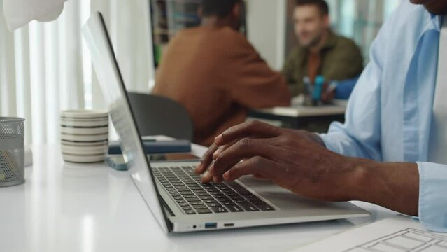 Cropped shot of hands of unrecognizable programmer of African American ethnicity typing code on laptop at office desk