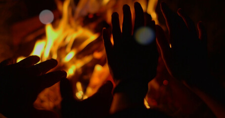 Silhouettes of hands in front of a burning fireplace in the dark