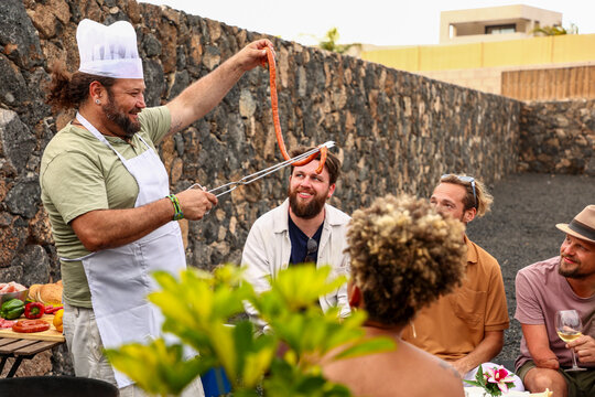 Cheerful chef grilling sausages at outdoor bbq party