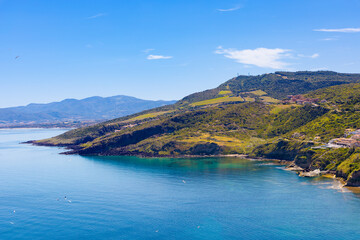 Obraz premium Vista panorámica de la costa de Castelsardo, Cerdeña, Italia El mar Tirreno, de un azul profundo, se extiende junto a colinas verdes y acantilados escarpados, ofreciendo un paisaje natural.