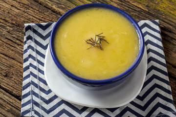 Delicious cassava cream (Caldo ou Creme de Mandioca) or cassava soup, typical of Brazilian cuisine, served in a blue porcelain bowl, on top of a typical rustic farm table, top view with selective focu