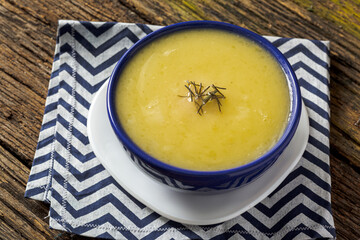 Delicious cassava cream (Caldo ou Creme de Mandioca) or cassava soup, typical of Brazilian cuisine, served in a blue porcelain bowl, on top of a typical rustic farm table, top view with selective focu