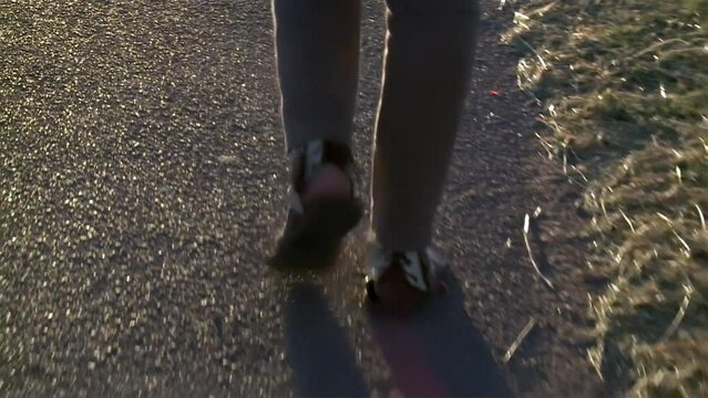 Low-angle View of a Woman Walking Along an Asphalt Path in a Park at Sunset.