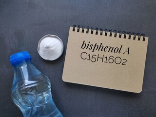 Chemical formula of bisphenol A written in notebook with white bisphenol A powder and plastic...