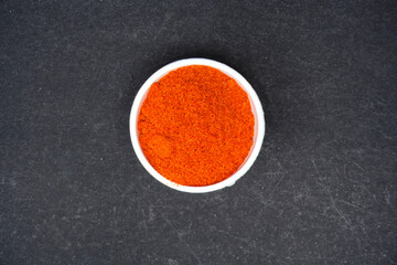 top view of red chili pepper powder in white bowl, isolated in black background