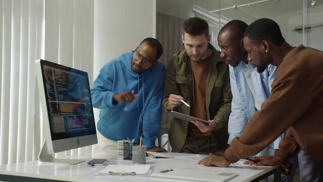 Medium long shot of diverse IT specialists searching for bags in programming code looking at screen of computer at office