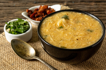 Caldo de Kenga Cassava broth with shredded chicken, typical Brazilian food known as (Caldo de Quenga), in a black pot on top of a rustica with a spoon and slices of bread,  with selective focus