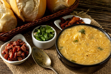 Caldo de Kenga Cassava broth with shredded chicken, typical Brazilian food known as (Caldo de Quenga), in a black pot on top of a rustica with a spoon and slices of bread,  with selective focus
