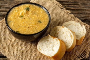Caldo de Kenga Cassava broth with shredded chicken, typical Brazilian food known as (Caldo de Quenga), in a black pot on top of a rustica with a spoon and slices of bread,  with selective focus