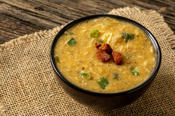 Caldo de Kenga Cassava broth with shredded chicken, typical Brazilian food known as (Caldo de Quenga), in a black pot on top of a rustica with a spoon and slices of bread,  with selective focus