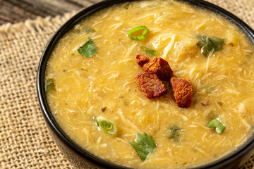 Caldo de Kenga Cassava broth with shredded chicken, typical Brazilian food known as (Caldo de Quenga), in a black pot on top of a rustica with a spoon and slices of bread,  with selective focus