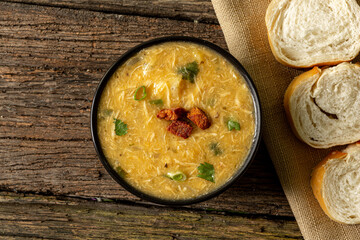 Caldo de Kenga Cassava broth with shredded chicken, typical Brazilian food known as (Caldo de Quenga), in a black pot on top of a rustica with a spoon and slices of bread,  with selective focus
