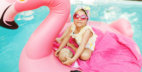 Cute funny toddler girl in colorful swimsuit and sunglasses relaxing on inflatable toy ring...