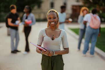 Close up of diverse female student with textbook at campus smiling.