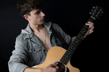 Obraz premium Shirtless young man in denim jacket playing guitar in photo studio