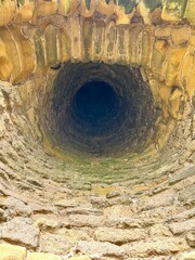 A view looking down an old stone well with moss-covered walls, creating a deep, dark tunnel.