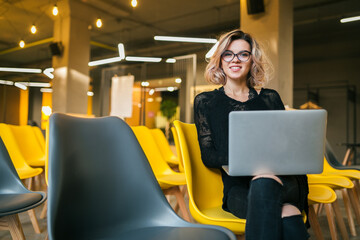 portrait of young attractive woman sitting in lecture hall working on laptop