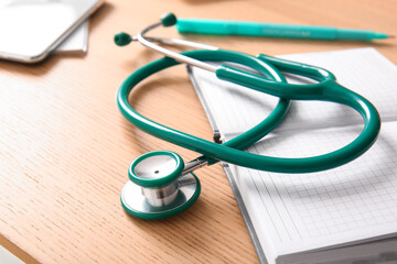 Notebook with stethoscope on wooden medical desk, closeup