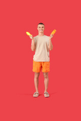 Happy young man with bottles of sunscreen cream on red background