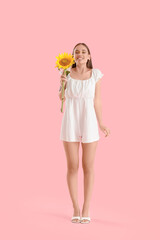 Young happy woman with beautiful sunflower on pink background
