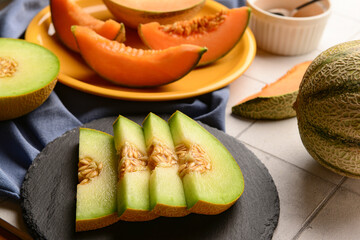 Slate board with slices of tasty ripe melon on white tile background