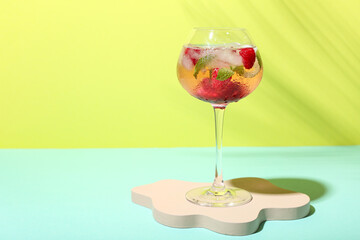 Decorative podium with glass of fresh raspberry mojito on colorful background