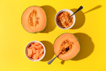 Halves of sweet melon and bowls with pieces on yellow background