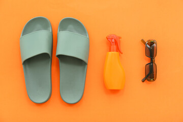 Pair of green flip flops with sunscreen spray and sunglasses on orange background